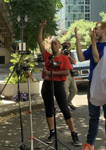 Demetria Hester standing with a fist raised in front of press conference microphones