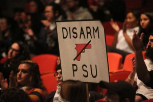 Students hold up a sign that reads "Disarm PSU" at an assembly