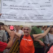 white woman, gray hair, red t-shirt, smiling, holding up sign (illegible)